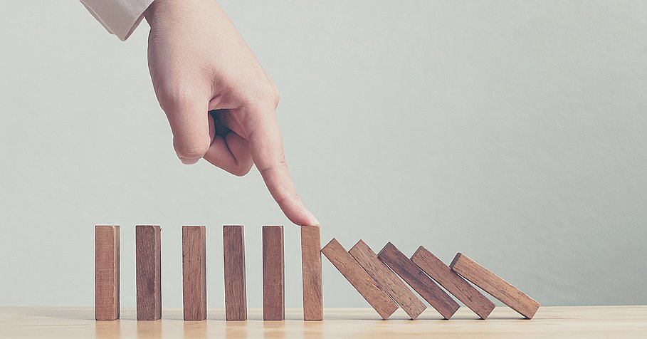 Hand stopping wooden domino business crisis effect or risk protection concept